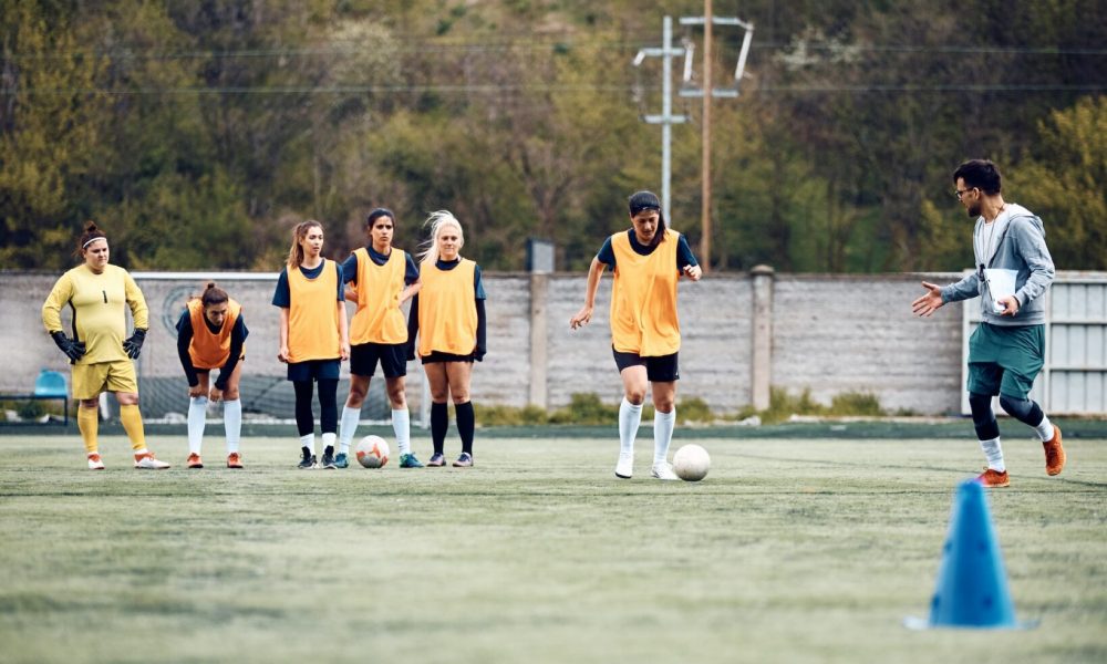 Soccer coach and female players during sports training on playing field.